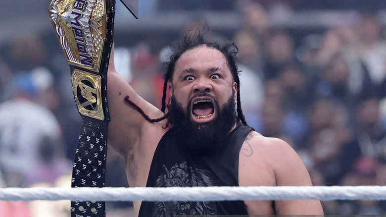 Jacob Fatu hangs his mouth open with wild eyes as he hoists the United States Championship title above his head.