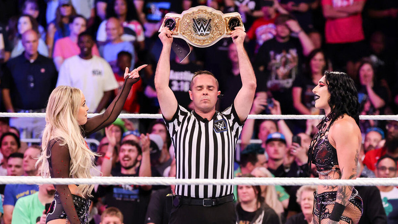 Liv Morgan and Rhea Ripley stand across the ring from each other with the referee holding up the Women's World Championship before a match. each other with the